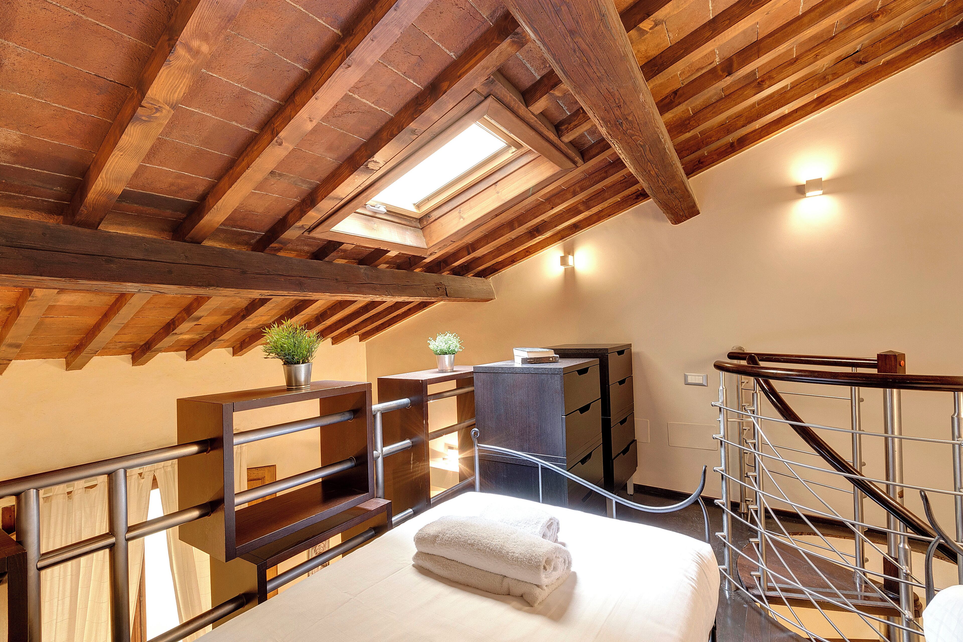 A bedroom with a skylight, a bed with a rolled-up towel, a dresser, and a staircase with a metal railing.