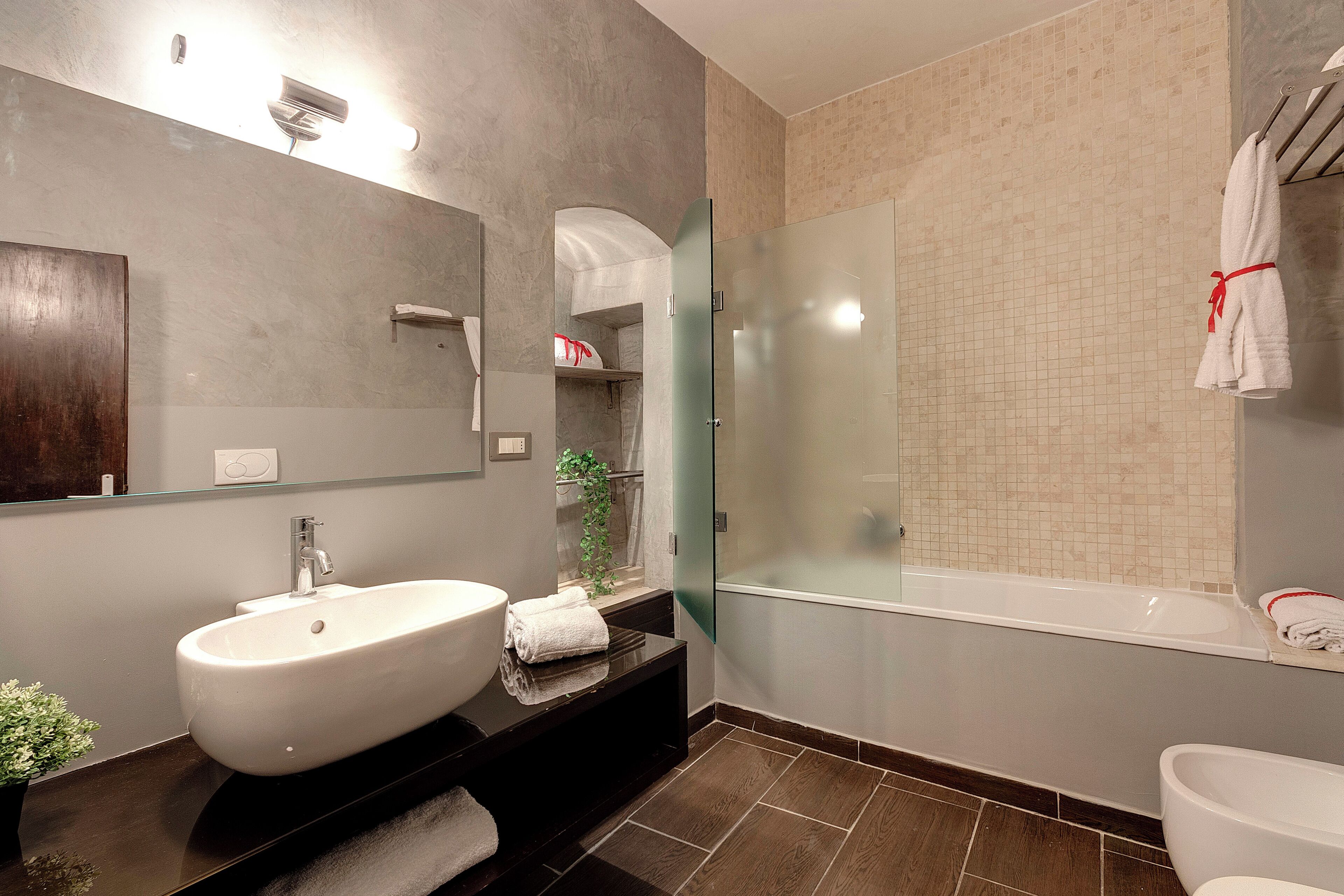 A modern bathroom with a large white sink, a glass-enclosed shower, and a bathtub.