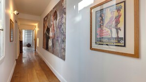 A hallway with wooden flooring, a large abstract painting on the left, and a framed poster on the right.