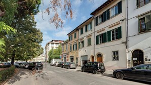 A street lined with parked cars and buildings with green shutters.