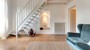 A modern living room with a staircase, a blue sofa, and a rug.