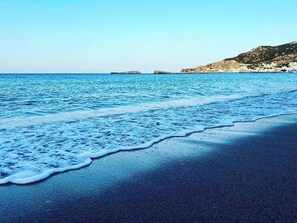 A beach with waves gently lapping onto the shore, a clear sky, and a rocky coastline in the background.