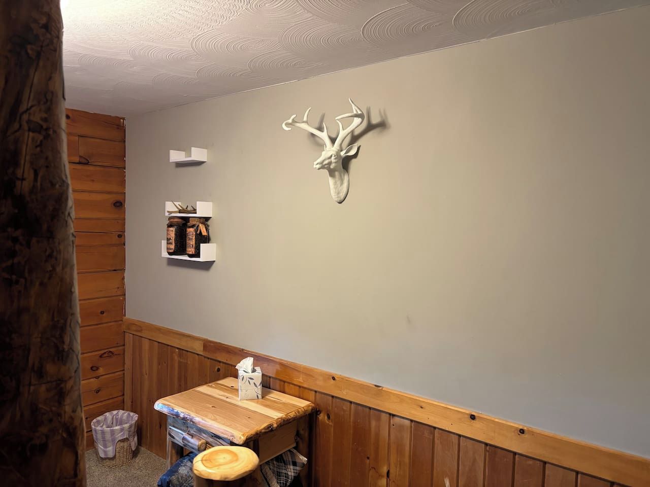 A bathroom with wooden paneling, a wooden bench, a wall-mounted deer head decoration, and a shelf with toiletries.