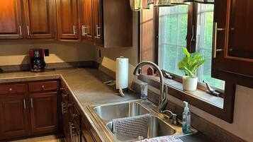 A kitchen with wooden cabinets, a stainless steel sink, a coffee maker, and a window with a curtain.