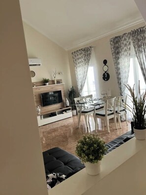 A modern living room with a flat-screen TV, a dining area with a glass table and white chairs, and a black sofa. - Guesthouse Milagre Centro Faro (Faro)