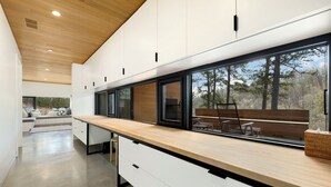 Een moderne keuken met een houten aanrechtblad, witte kasten en grote ramen met uitzicht op de omgeving.