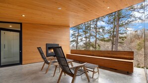 Een modern interieur met een houten plafond, een groot raam met uitzicht op een bos en een in de muur gebouwde open haard.
