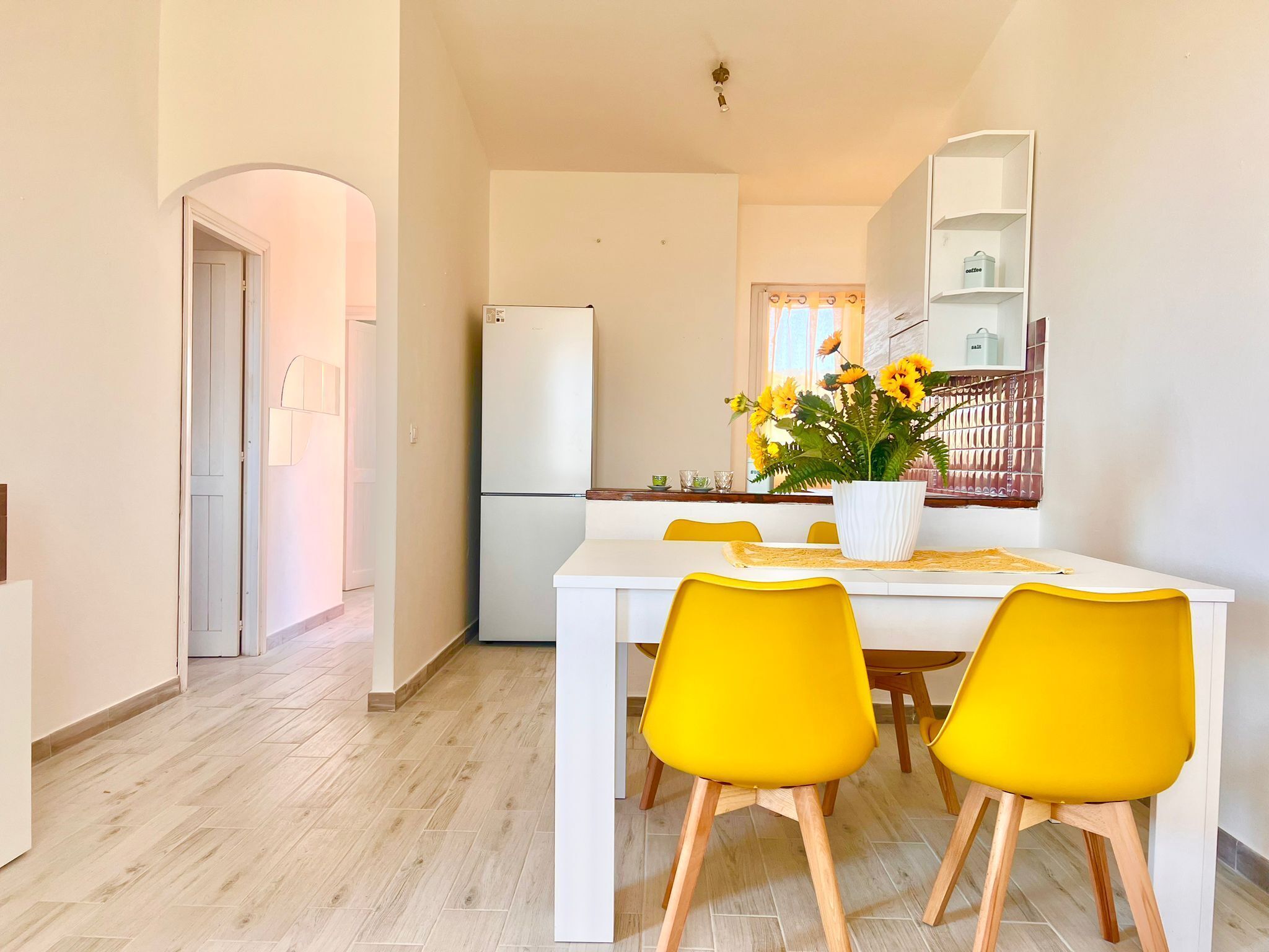 A modern kitchen with a white refrigerator, yellow chairs, and a dining table.
