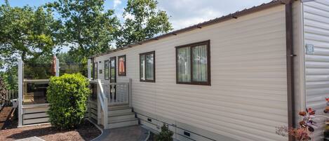 A mobile home with a covered porch, a small garden area, and a paved walkway.