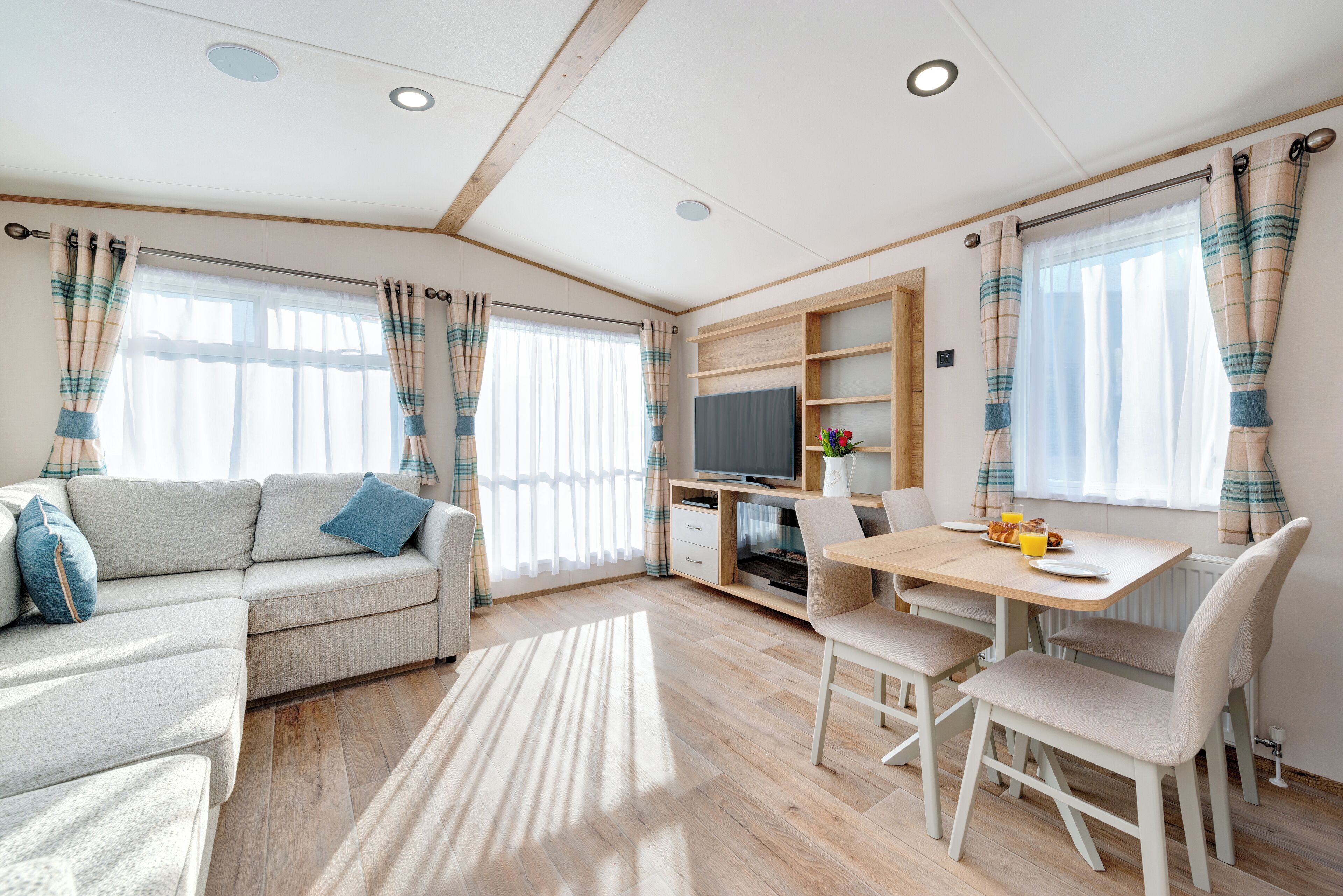 A modern living room with a sofa, a dining table with chairs, a TV, and a bookshelf.