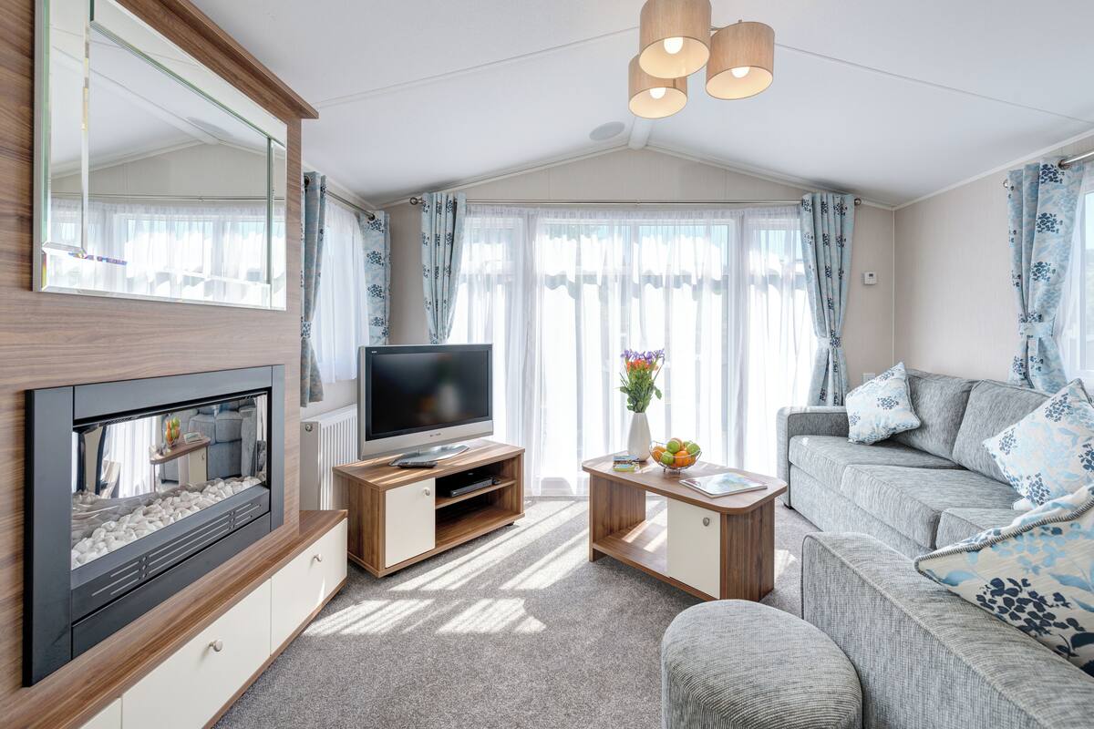 Ein modernes Wohnzimmer mit einem Flachbildfernseher auf einem Holzständer, einer Couch, einem Couchtisch und einem Kamin.
