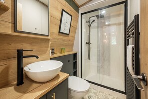 A modern bathroom with a wooden vanity, a white sink, a toilet, and a glass-enclosed shower.