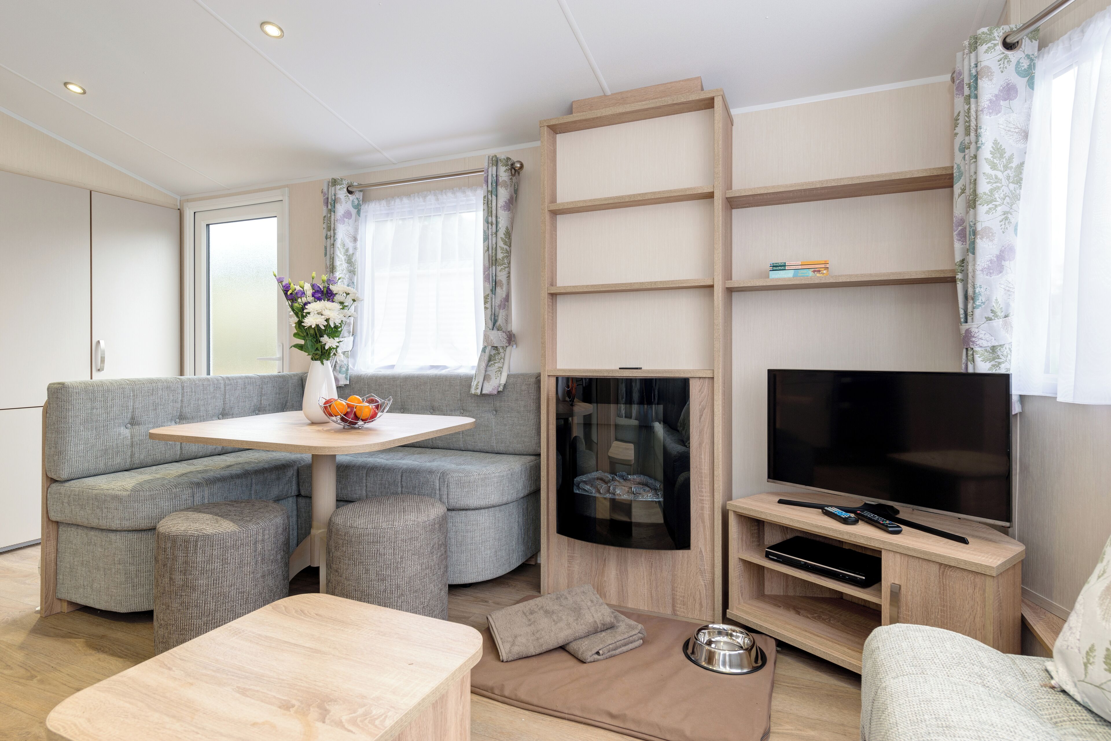 Ein modernes Wohnzimmer mit Sofa, Esstisch, Fernseher und integrierten Regalen.
