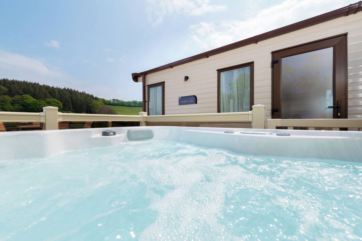 Ein Whirlpoolbereich mit Blick auf einen bewaldeten Hügel, eine Holzterrasse und ein Gebäude mit großen Fenstern und einem Schild.