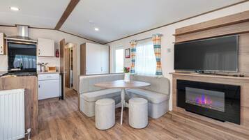 A modern kitchen with a built-in stove, a dining area with a round table and two stools, and a large TV mounted above a fireplace.
