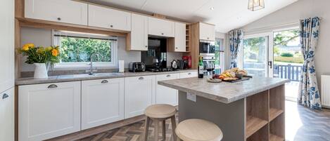 A modern kitchen with white cabinets, a central island with stools, a window with a view of greenery, and a herringbone floor pattern.