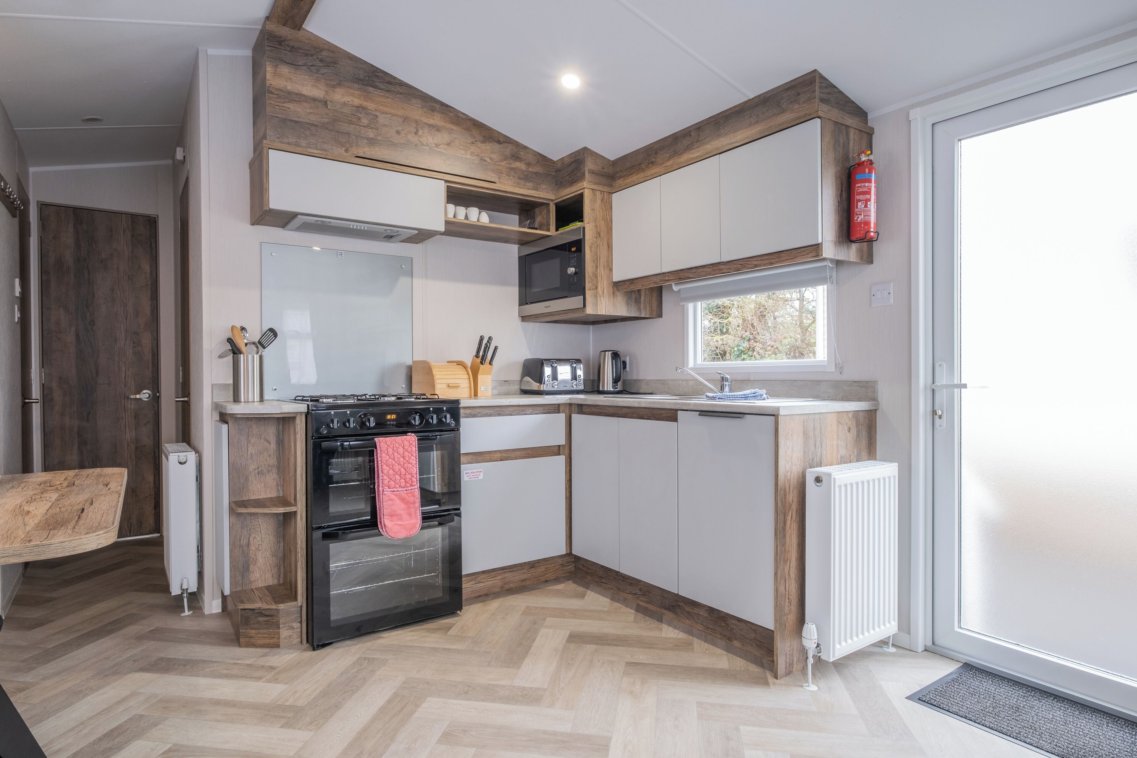 A compact kitchen with a built-in oven, microwave, and toaster. There is a wooden countertop and a window providing natural light.
