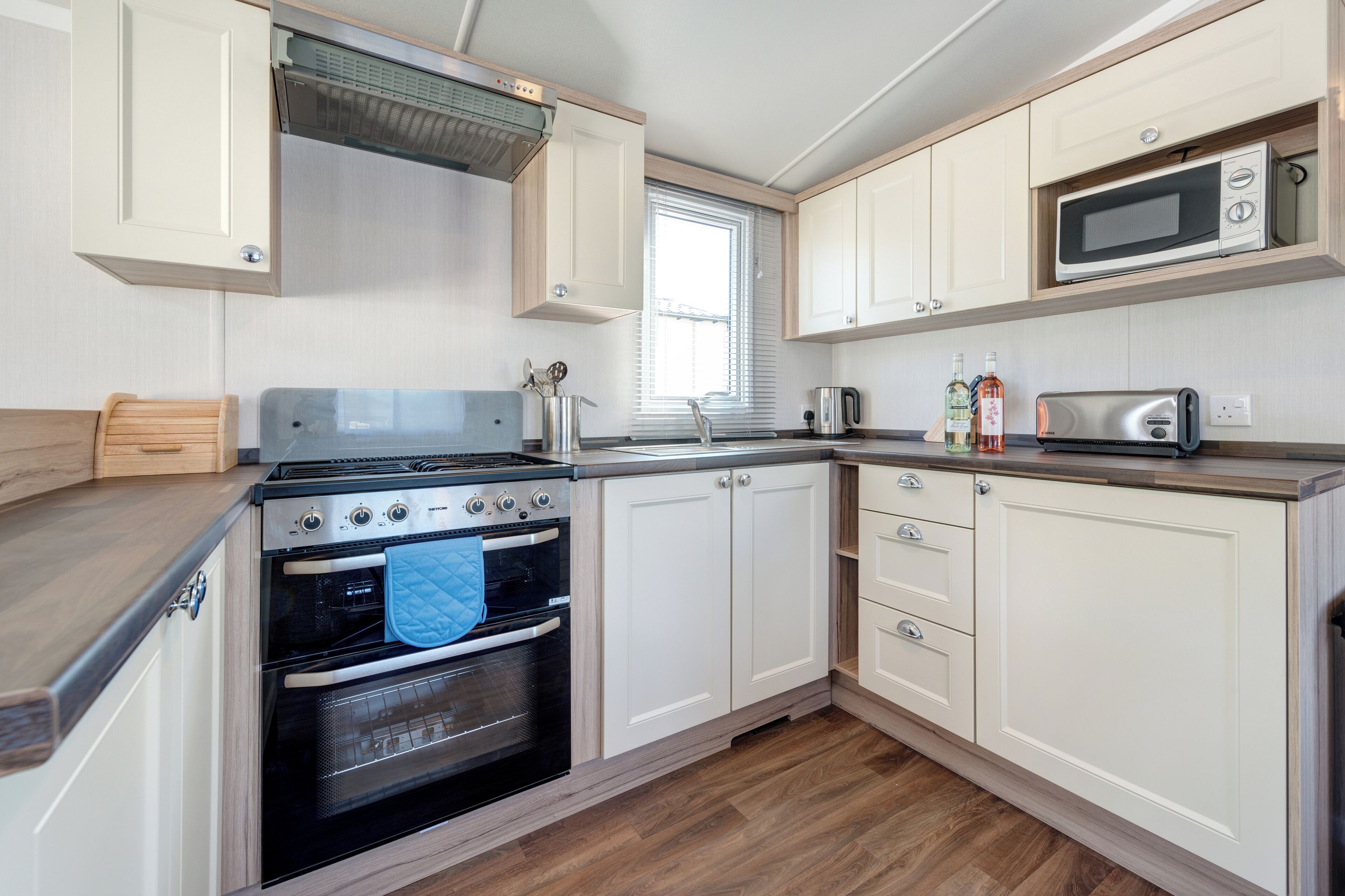 A compact kitchen with a stove, oven, microwave, and wooden cabinets.