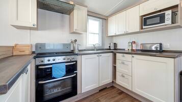 A compact kitchen with a stove, oven, microwave, and wooden cabinets.