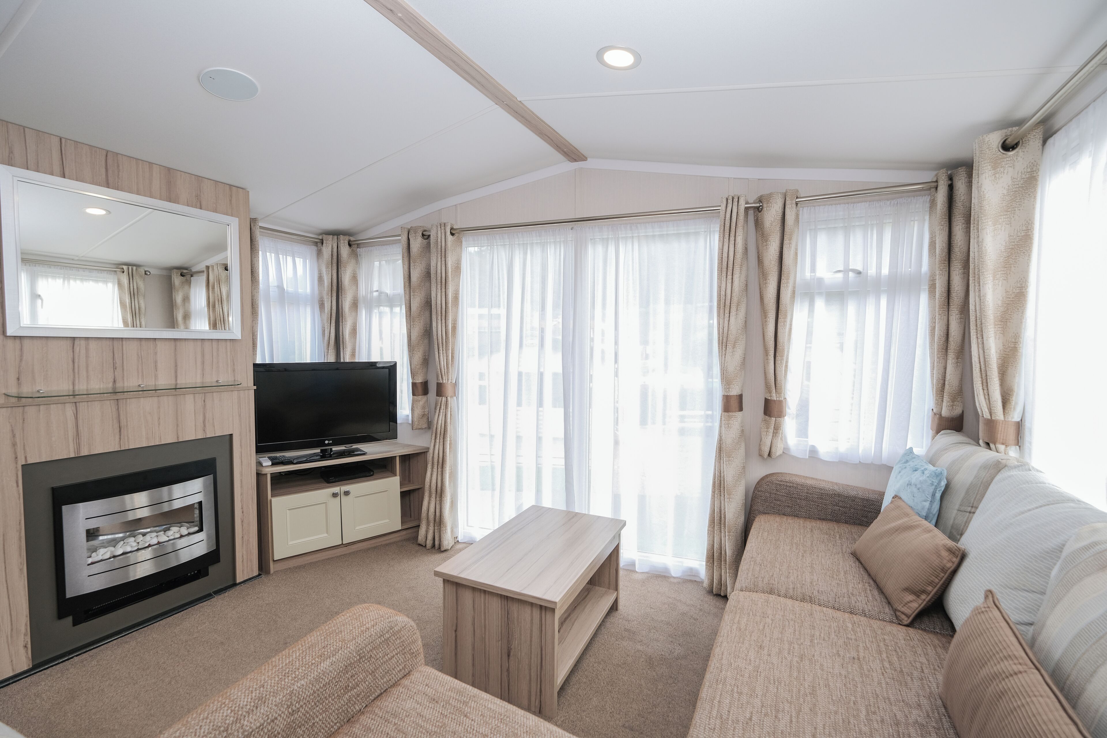 A living room with a flat-screen TV, a fireplace, a sofa, and a large window with curtains.