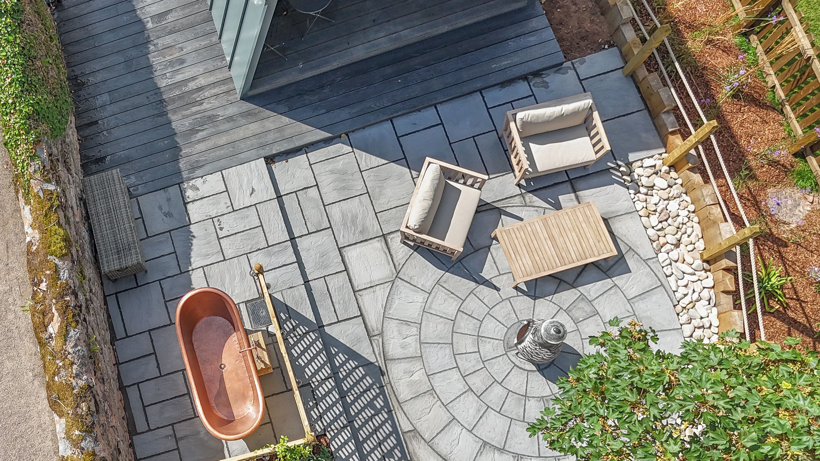 A patio with a hot tub, two wicker chairs, a wooden table, and a decorative metal sculpture.