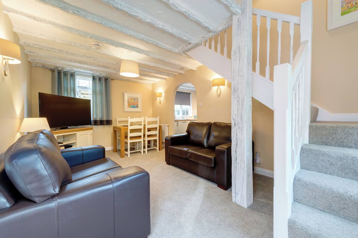 Ein Wohnzimmer mit einer Couch, einem Fernseher, einem Essbereich und einer Treppe.
