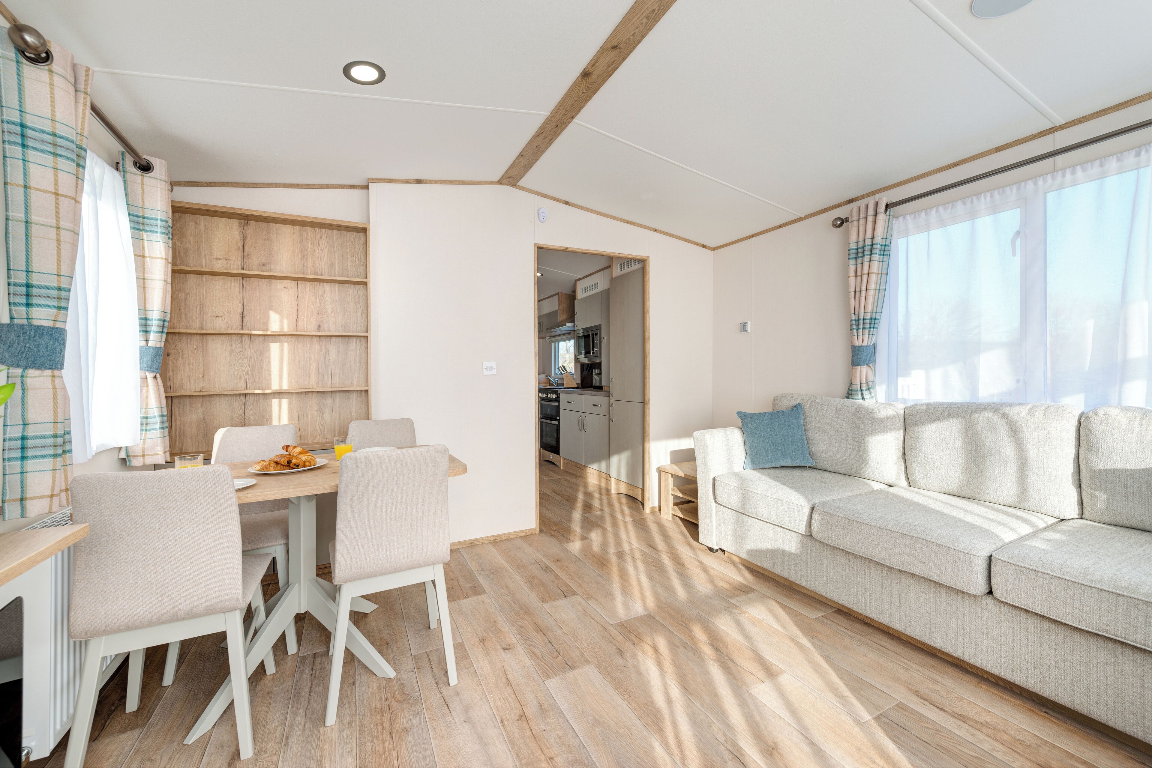 Ein modernes Wohnzimmer mit einer Couch, einem Esstisch und Stühlen. Im Hintergrund ist eine Küche erkennbar.