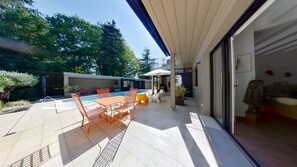 Eine moderne Außenpatio mit Pool, einem Essbereich mit orangefarbenen Stühlen und einer überdachten Sitzgruppe.