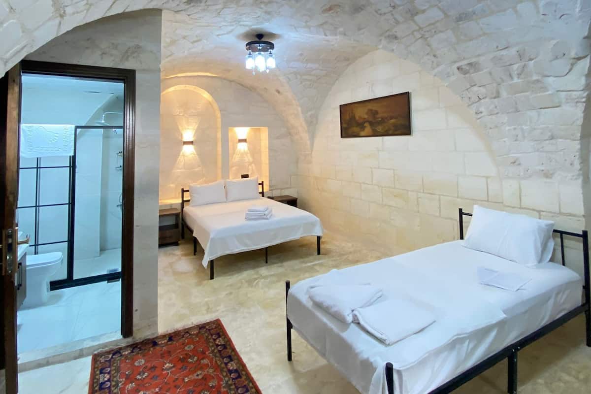 A room with a stone ceiling, two beds, a red carpet, and a bathroom visible through an archway.
