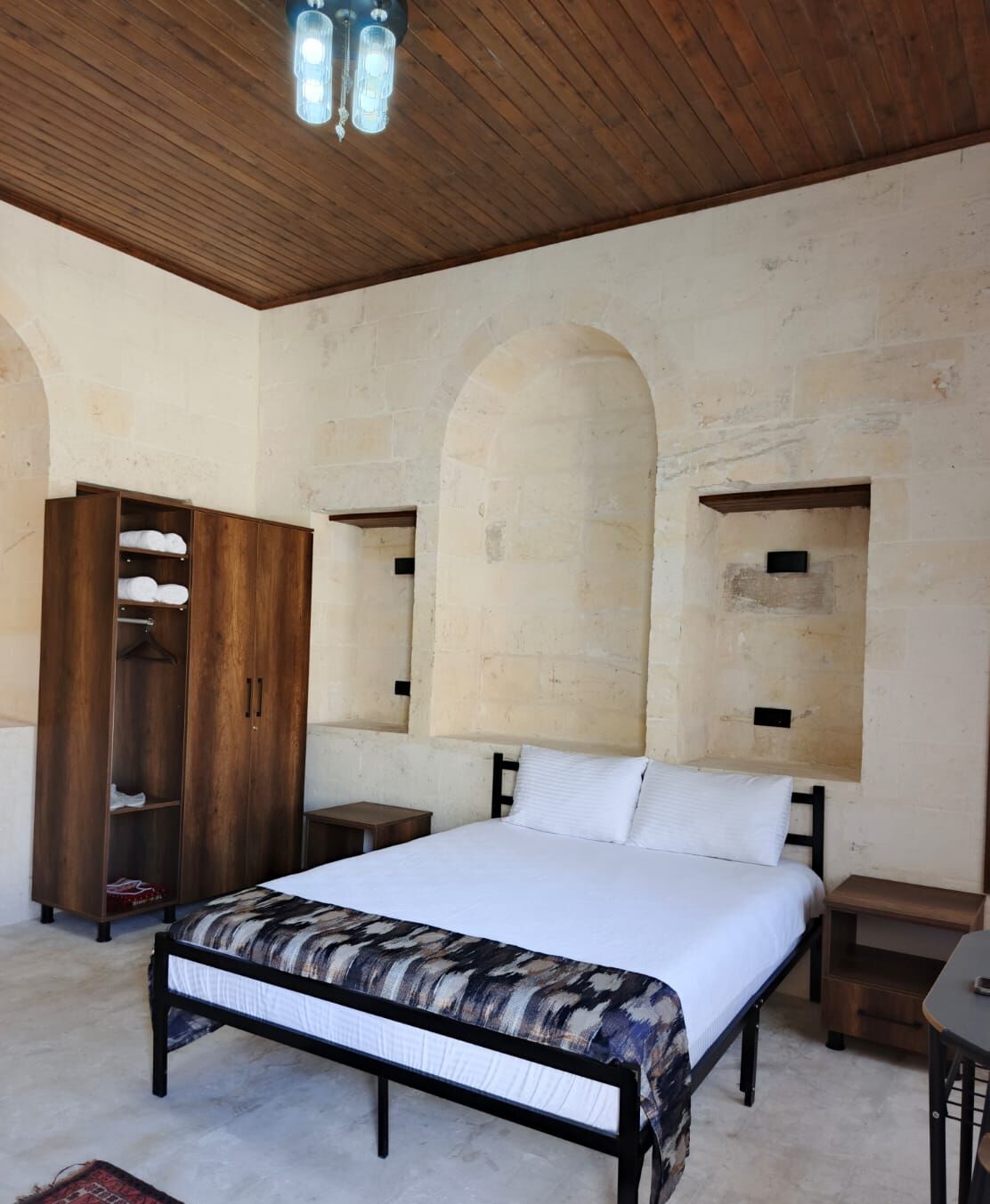 A bedroom with a bed, wooden wardrobe, and a stone wall with arched niches.