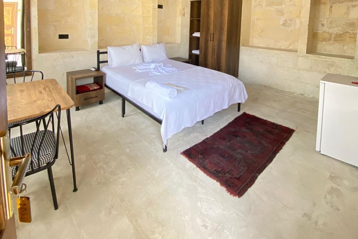A bedroom with a bed, a desk, a chair, and a small table.
