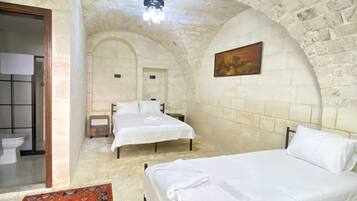 A room with two beds, a red patterned rug, stone walls, and a ceiling light.