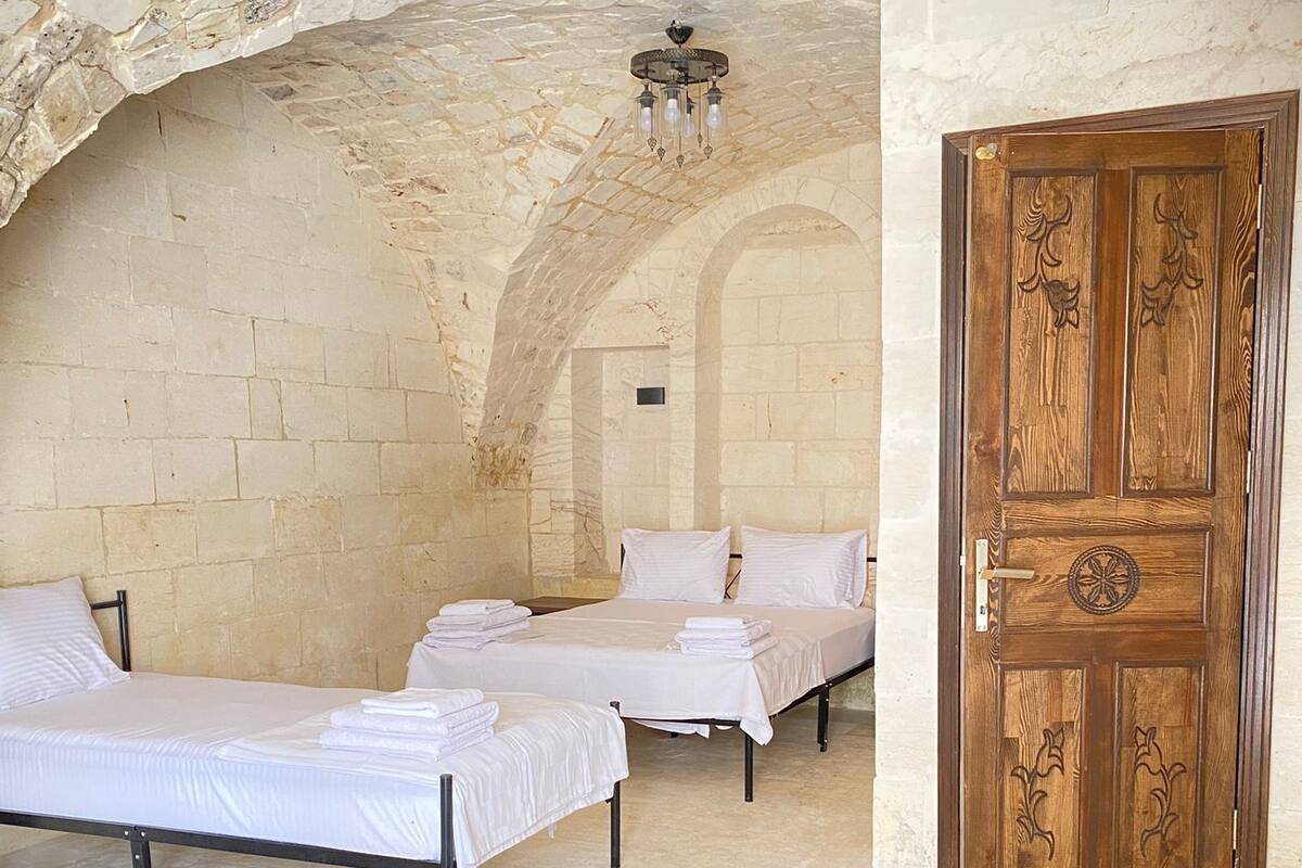 A room with three beds, a wooden door, and a red rug.