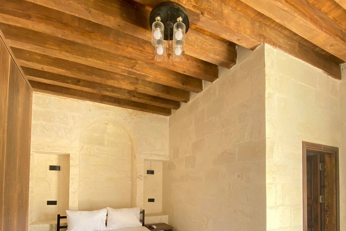 A bedroom with a large bed, wooden ceiling beams, stone walls, and a small rug.