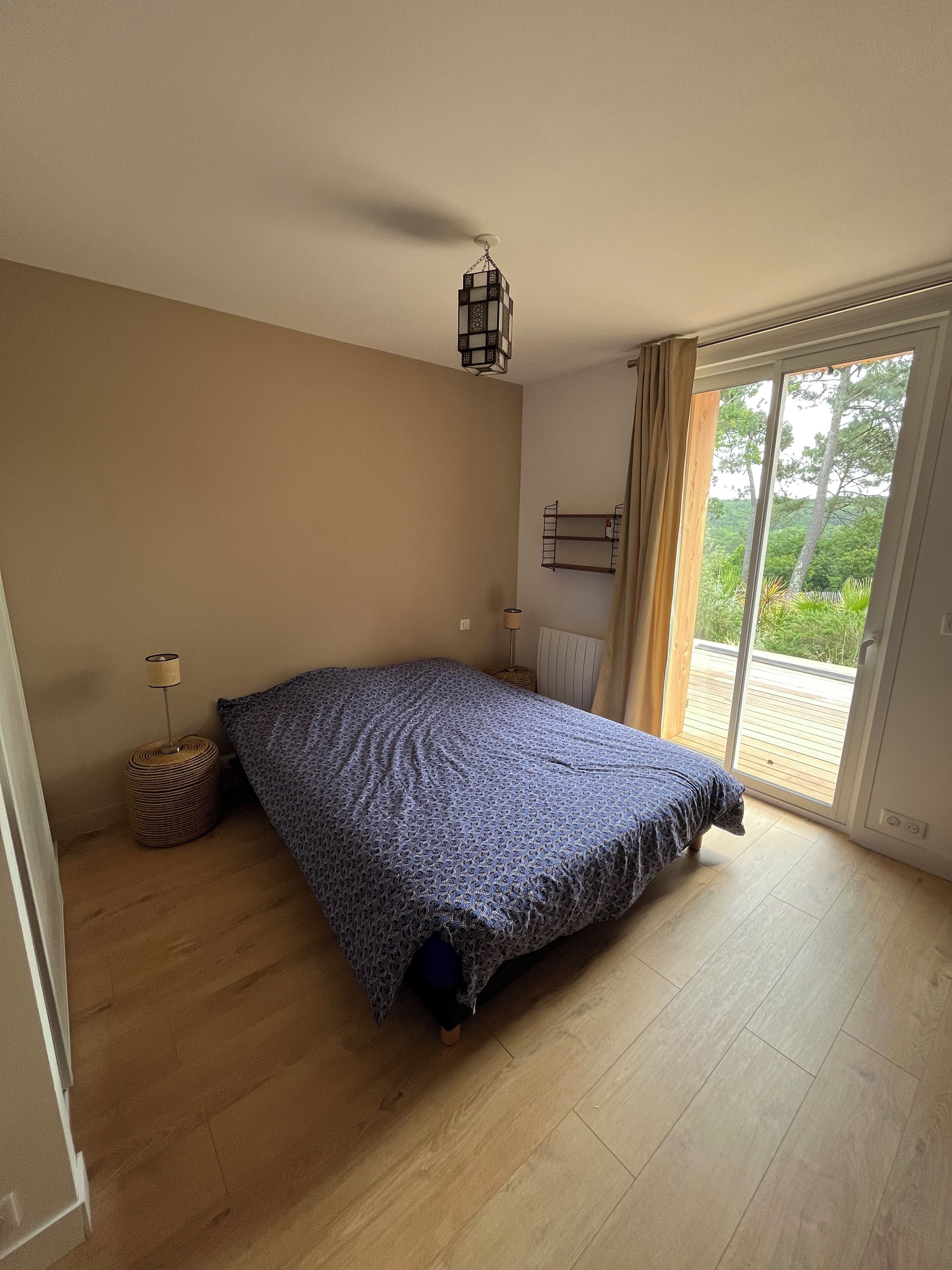 Une chambre à coucher avec un lit, une lampe, un radiateur et une vue sur la verdure, visible à travers une porte coulissante.