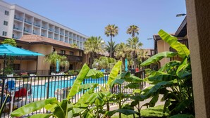 A hotel with a swimming pool, palm trees, and a clear blue sky.