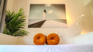 A room with a bed, a wall-mounted painting of a lighthouse, and a potted plant. - Flamingos Hideaway  (South Padre Island)
