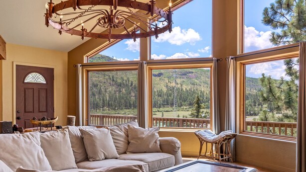 Ein großzügiger Wohnraum mit einem großen Fenster und Blick auf die Berge, einem gemütlichen Sofa und einem Holztisch.