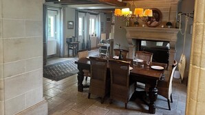 Een eethoek met een houten tafel en rieten stoelen, een kroonluchter en een open haard.