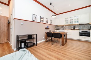 A compact kitchen with white cabinets, a wooden dining table, and a black TV stand.