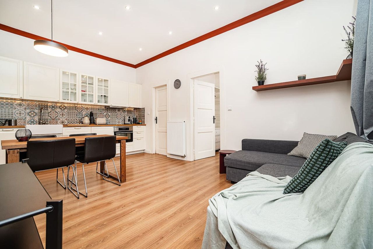 Una cocina moderna con armarios blancos, una mesa de comedor de madera y sillas. Hay un sofá gris y una pequeña mesita auxiliar en la sala.