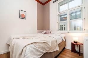 A bedroom with a bed, a bedside table with a lamp, a window with a view of the outside, and a framed picture on the wall. - Charming, modern, 1-bed flat by Museum of Prague (Praha 8)