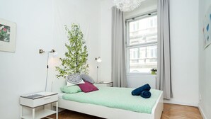 A minimalist bedroom with a bed, bedside tables, a window with curtains, and a plant.