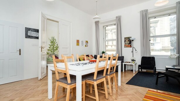 A modern living room with a white dining table, wooden chairs, a black sofa, a small side table, and a floor lamp.