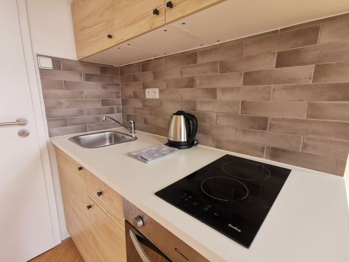 A compact kitchen with a white countertop, a black induction cooktop, a kettle, and a sink.