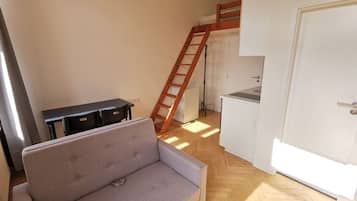 A compact living space with a sofa, a small table, a ladder, and a kitchenette.
