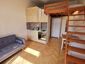 A compact living space with a kitchenette, a sofa, and a wooden loft bed. - Modern studio with excellent transport links (Praha 10)
