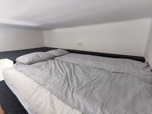 A single bed with a patterned bedspread and pillows, a white wall, and a power outlet. - Modern studio with excellent transport links (Praha 10)