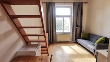 A room with a wooden staircase, a sofa, a radiator, and a window with curtains.