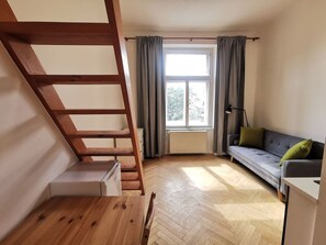 A room with a wooden staircase, a sofa, a radiator, and a window with curtains. - Modern studio with excellent transport links (Praha 10)